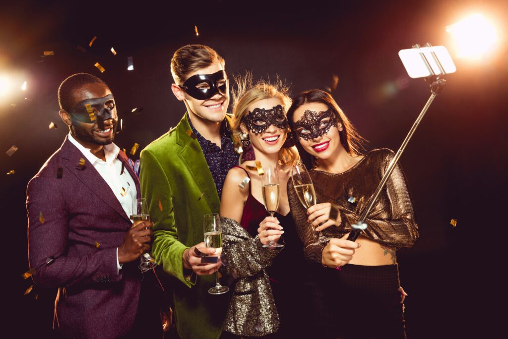 glamorous multicultural friends in carnival masks taking selfie on smartphone